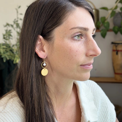 Woman wearing a white sweater and yellow leather statement earrings featuring gold-plated rings and crystal details, seated indoors.