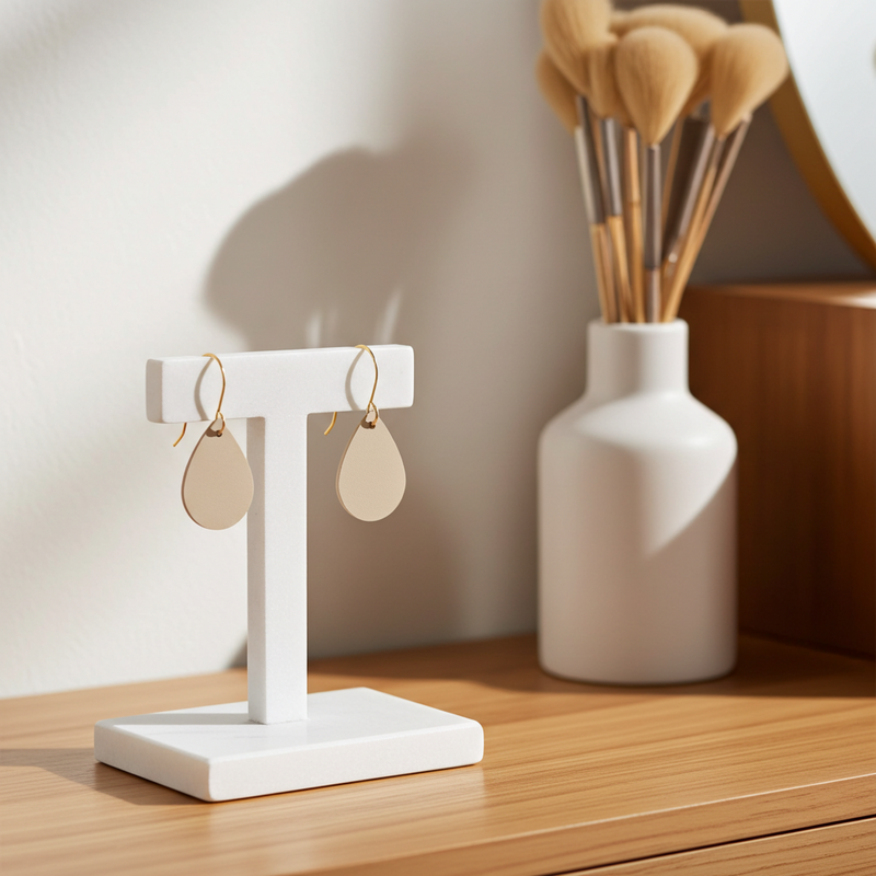 Beige leather teardrop earrings with gold-plated hooks on a white stand with a vase in the background.