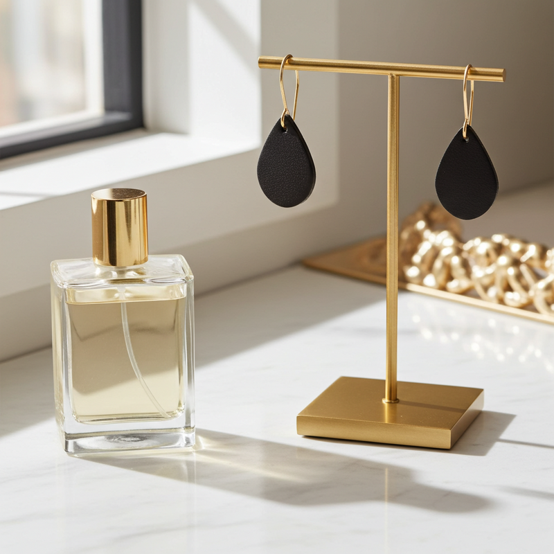 Gold perfume bottle and black leather earrings on a gold stand with a light background.