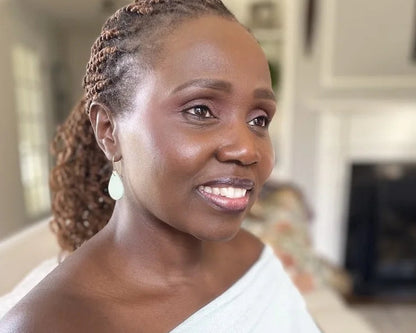 Woman with braided hair wearing seafoam green teardrop earrings with gold-plated hooks and half shoulder top in an indoor setting