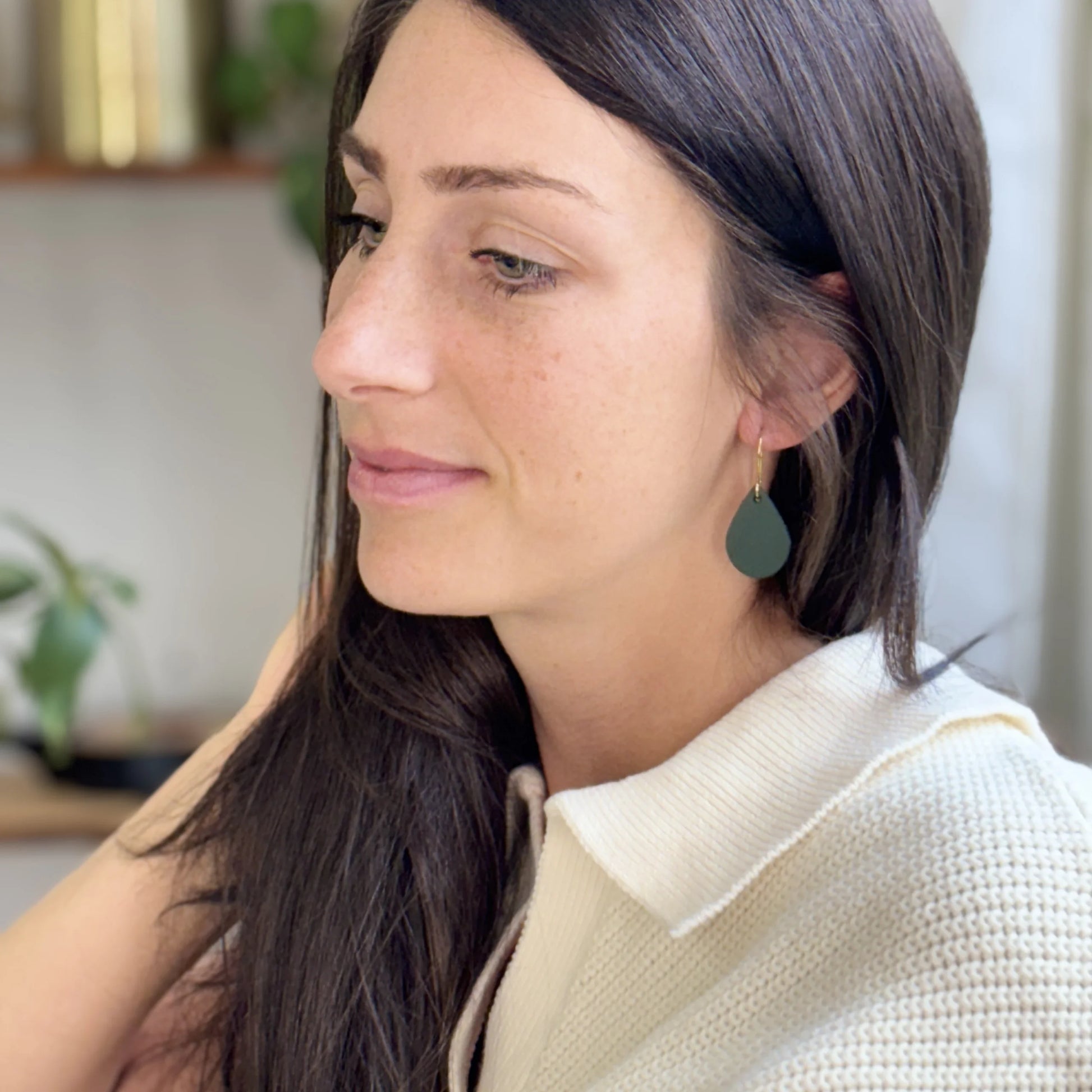 Woman wearing green leather teardrop earrings with gold-plated hooks in a casual setting.