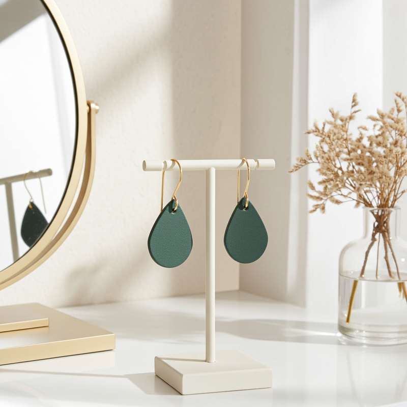 Green leather teardrop earrings with gold-plated hooks on a stand with a mirror and vase in the background.