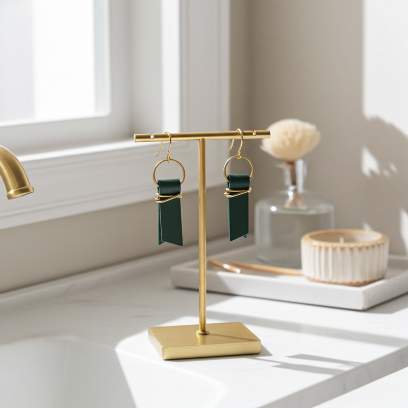 Green leather ribbon earrings accented with gold-plated wire and rings on a gold earring stand sitting on a light surface.