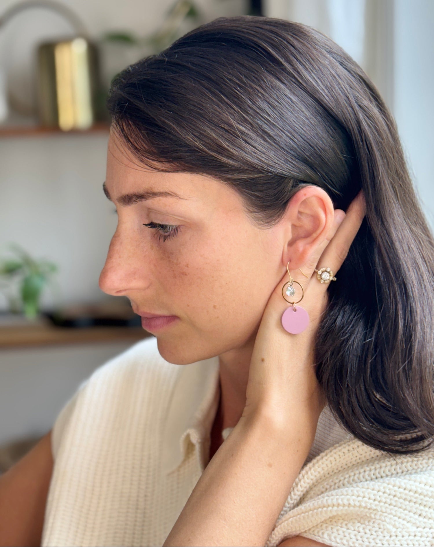 Woman wearing mauve leather statement earrings featuring gold-plated rings and crystal details in a neutral background.