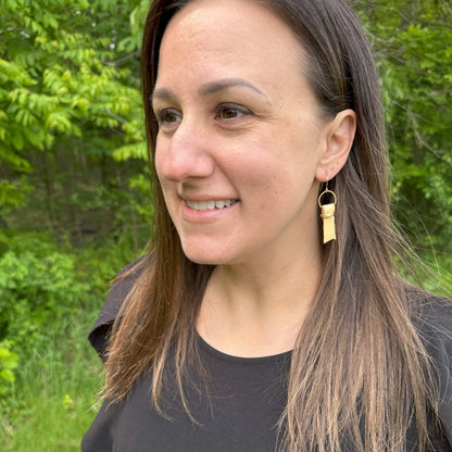 Woman with long brown hair wearing a black shirt and yellow leather ribbon earrings accented with gold-plated wire and rings, standing outdoors.