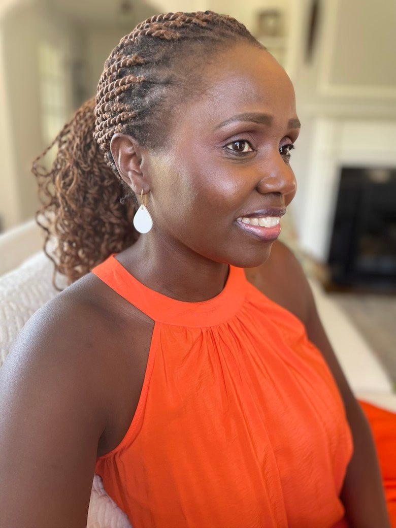 Woman wearing an orange top sitting on a couch wearing white leather teardrop earrings