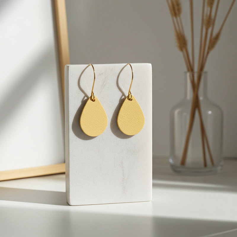Yellow leather teardrop earrings with gold-plated hooks on a white stand with a minimal background.