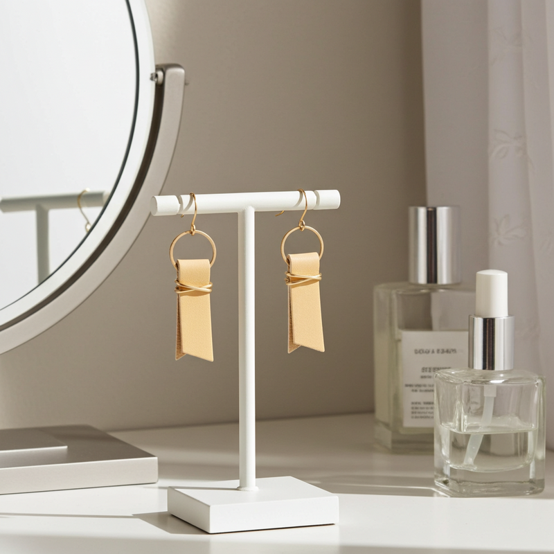 Yellow leather ribbon earrings accented with gold-plated wire and rings on a stand with perfume bottles in the background.